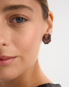 Los pendientes Roaring, inspirados en la vibrante energía de los 'Roaring Twenties', están fabricados en plata de ley 925 con un elegante baño de rodio negro. Su diseño en forma de flor, adornado con circonitas en tonalidad granate, aporta un estilo único y moderno. Con cierre de tuerca, estos pendientes son ideales para quienes buscan una pieza audaz y sofisticada que combine lujo con un toque diferente.